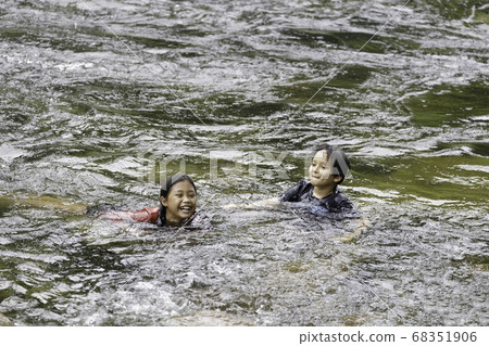 A pair of elementary school boys and girls play in the rushing stream 68351906