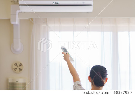 [Summer image] A young woman operating a room air conditioner in the living room with a remote control 68357959