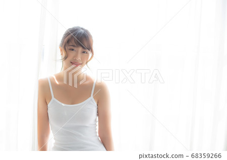 Portrait of beautiful young asian woman standing the window and smile while wake up with sunrise. Portrait of beautiful young asian woman standing the window and smile while wake up with sunrise. 68359266