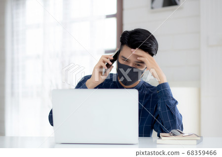 Young asian business man in face mask talking smartphone and work on laptop computer for protect. 68359466
