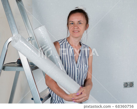 A happy woman holds rolls of new Wallpaper in her hands. Repairs in the apartment. Wallpapering. A happy woman holds rolls of new Wallpaper in her hands. Repairs in the apartment. Wallpapering. 68360756