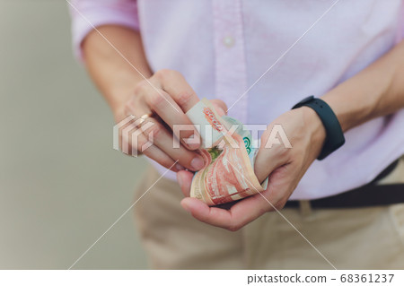 A close up photo of a Caucasian male hand holding a 100 Russian ruble note. 68361237