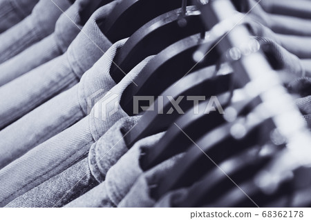 Row of denim jackets or shirts on black hangers, a top view closeup. Jeans wardrobe. Blue textile background, blurry (shallow depth of field). 68362178