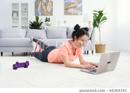 The girl trains at home online with elastic bands for fitness. Online home training for a woman with a laptop. Sports at home under quarantine. The girl trains at home online with elastic bands for fitness. Online home training for a woman with a laptop. Sports at home under quarantine. 68364341