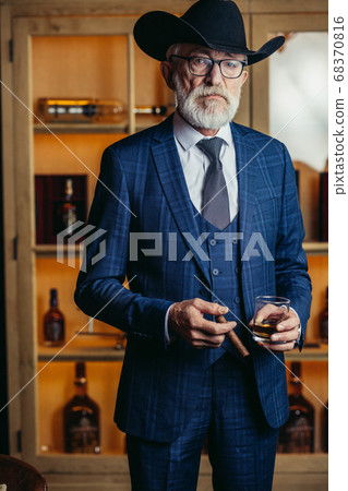 Portrait of old-aged male dandy in big hat smokes cigar and drin 68370816