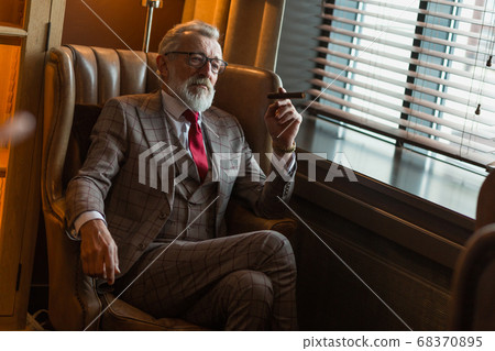 Serene concentrated mature male architector with grey-haired beard smoking cigar 68370895
