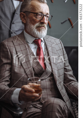 Bearded old businessman sitting at barber shop in chair choosing haircut design 68373222