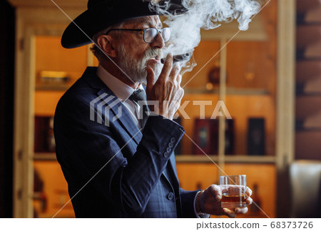 Portrait of old-aged male dandy in big hat smokes cigar and drin Portrait of old-aged male dandy in big hat smokes cigar and drin 68373726