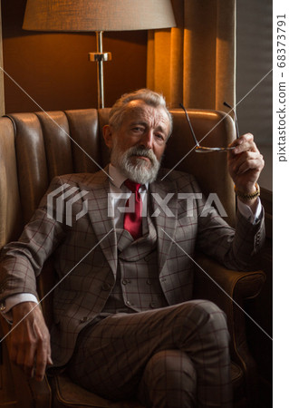 Satisfied bearded pensioner adjusting spectacles while resting in apartment. Satisfied bearded pensioner adjusting spectacles while resting in apartment. 68373791