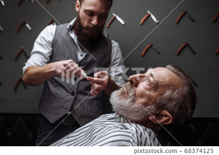 Old man getting his beard shaved by barber Old man getting his beard shaved by barber 68374125