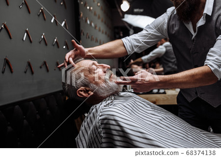 Old man getting his beard shaved by barber Old man getting his beard shaved by barber 68374138