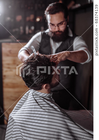 Skillful barber. Young man getting an old-fashioned shave with s Skillful barber. Young man getting an old-fashioned shave with s 68374139