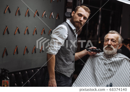 Hairdresser doing styling with the electric shaver for old man at barber shop 68374140