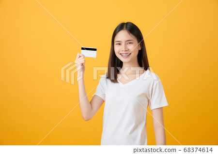 Attractive smiling Asian woman holding credit card payment on yellow background with copy space. 68374614