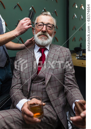 Bearded old businessman sitting at barber shop in chair choosing haircut design 68374664
