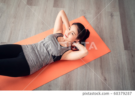 Asian woman wearing sportswear doing sit-up on orange mat in living room. Healthy lifestyle concept. 68379287