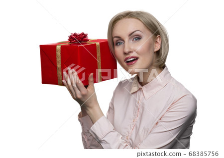 Curious young lady looking up and putting her ear to red gift box. 68385756