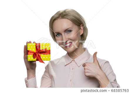 Happy smiling blond woman holding gift box and making ok gesture. 68385763