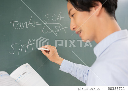 Young male teacher writing mathematical formula on blackboard Young male teacher writing mathematical formula on blackboard 68387721