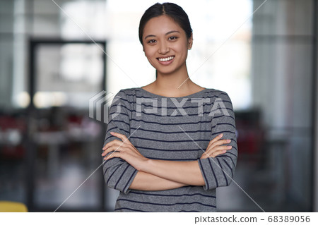 Portrait of a young happy asian woman, female office worker in casual clothes keeping arms crossed, looking at camera and smiling while standing in the modern office Portrait of a young happy asian woman, female office worker in casual clothes keeping arms crossed, looking at camera and smiling while standing in the modern office 68389056