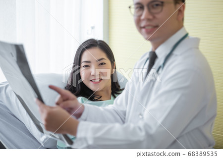 Asian female patient looking at camera and there was male doctor pointing at the x-ray. 68389535