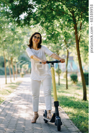 Joyful adorable senior woman using a scooter while riding in the park. Modern woman, a new generation. Healthy cheerful senior retired lady. Concept of Age Inclusivity and ecological transport Joyful adorable senior woman using a scooter while riding in the park. Modern woman, a new generation. Healthy cheerful senior retired lady. Concept of Age Inclusivity and ecological transport 68389958