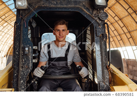 A man in overalls driving a tractor. Worker 68390581