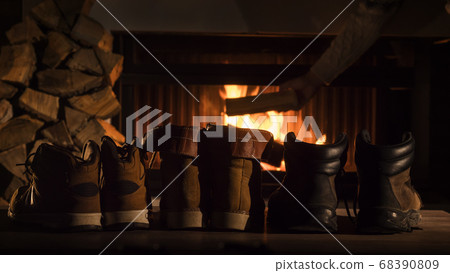 Shoes are drying by the fireplace, in the background a man throws firewood into a firebox Shoes are drying by the fireplace, in the background a man throws firewood into a firebox 68390809