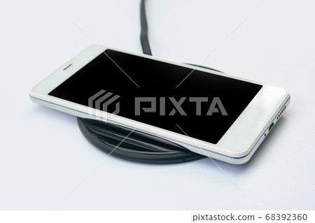 Smartphone charging on a wireless charger on white 68392360