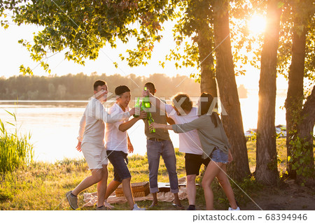 Group of friends clinking beer bottles during picnic at the beach. Lifestyle, friendship, having fun, weekend and resting concept. Group of friends clinking beer bottles during picnic at the beach. Lifestyle, friendship, having fun, weekend and resting concept. 68394946