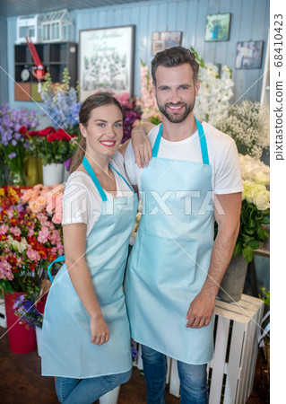 Bearded male and brown-haired female in aprons, embracing each other Bearded male and brown-haired female in aprons, embracing each other 68410423