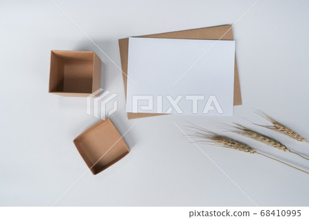 Blank white paper on brown paper envelope with Barle dry flower and Carton box. Mock-up of horizontal blank greeting card. Top view of Craft  envelope on white background. Flat lay minimalism 68410995