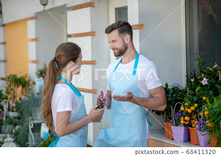 Bearded male and brown-haired female standing outside flower shop, talking Bearded male and brown-haired female standing outside flower shop, talking 68411320