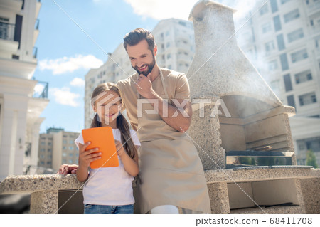 Dad and daughter watching something on a tablet and looking interested Dad and daughter watching something on a tablet and looking interested 68411708