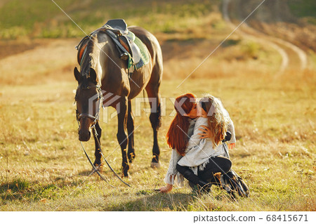 Mother and daughter in a field playing with a horse Mother and daughter in a field playing with a horse 68415671