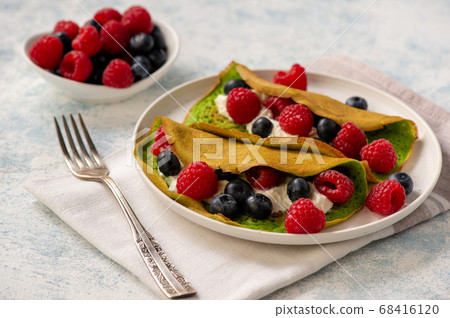 Spinach crepes with cheese , raspberries and blueberries. 68416120
