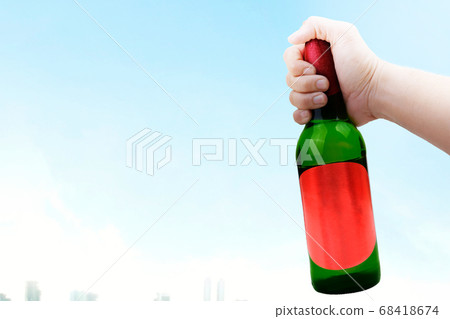 Hand holding beer bottle with a blue sky 68418674