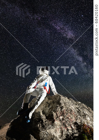 Spaceman sitting on rocky hill and looking at stars. 68420160