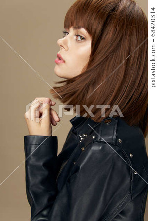 Young beautiful woman posing on a beige background in the studio in a black leather jacket Young beautiful woman posing on a beige background in the studio in a black leather jacket 68420314