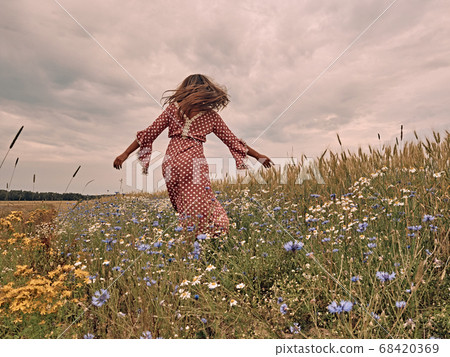 girl in a dress is spinning in the field. 68420369