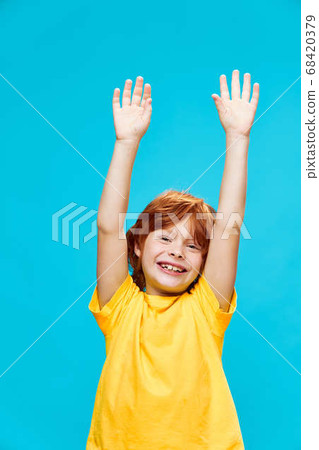 The red-haired boy with his hands raised up laughs on a blue background  The red-haired boy with his hands raised up laughs on a blue background  68420379