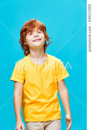 freckled red-haired child in yellow t-shirt smiling on blue background  68421069