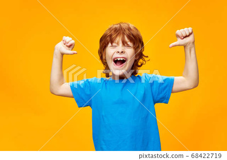 red-haired boy in a blue T-shirt is having fun on a yellow background and pointing at himself 68422719