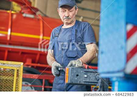 Attentive senior male person repairing big auto Attentive senior male person repairing big auto 68422983