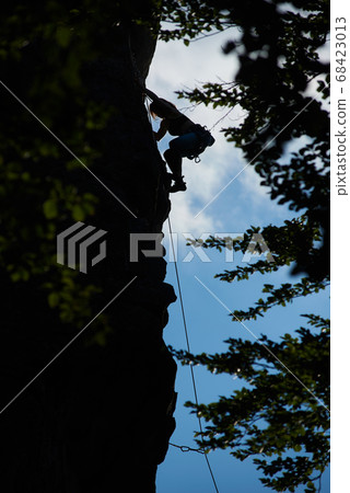 Low angle view silhouette of a girl in safety harness climbing up the rock against blue sky Low angle view silhouette of a girl in safety harness climbing up the rock against blue sky 68423013
