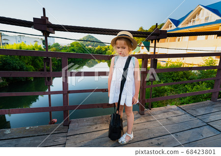 sad little girl with a heavy black bag on a bridge 68423801