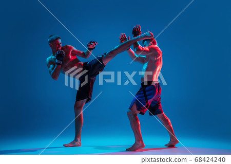 MMA. Two professional fighters punching or boxing isolated on blue studio background in neon MMA. Two professional fighters punching or boxing isolated on blue studio background in neon 68424240