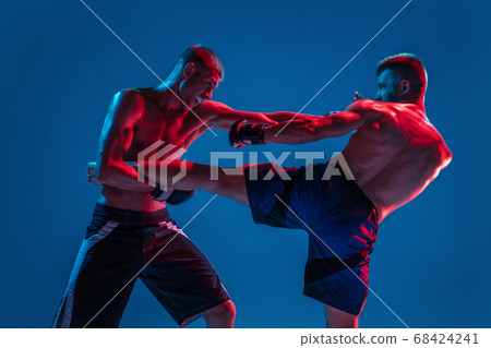 MMA. Two professional fighters punching or boxing isolated on blue studio background in neon MMA. Two professional fighters punching or boxing isolated on blue studio background in neon 68424241