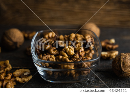 Walnut in a smale plate with scattered shelled nuts and whole nut which standing on a wooden vintage table. Walnuts is a healthy vegetarian protein nutritious food. Walnut on rustic old wood. 68424331
