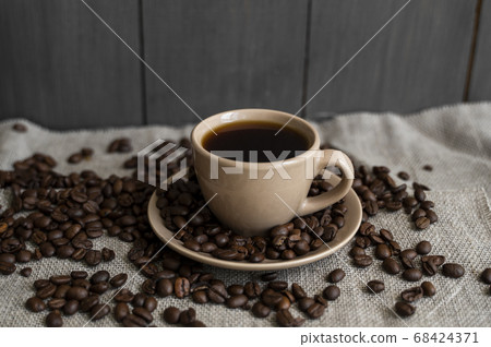 Coffee cup with roasted coffee beans on linen background. Mug of black coffe with scattered coffee beans. Fresh coffee beans. Coffee cup with roasted coffee beans on linen background. Mug of black coffe with scattered coffee beans. Fresh coffee beans. 68424371